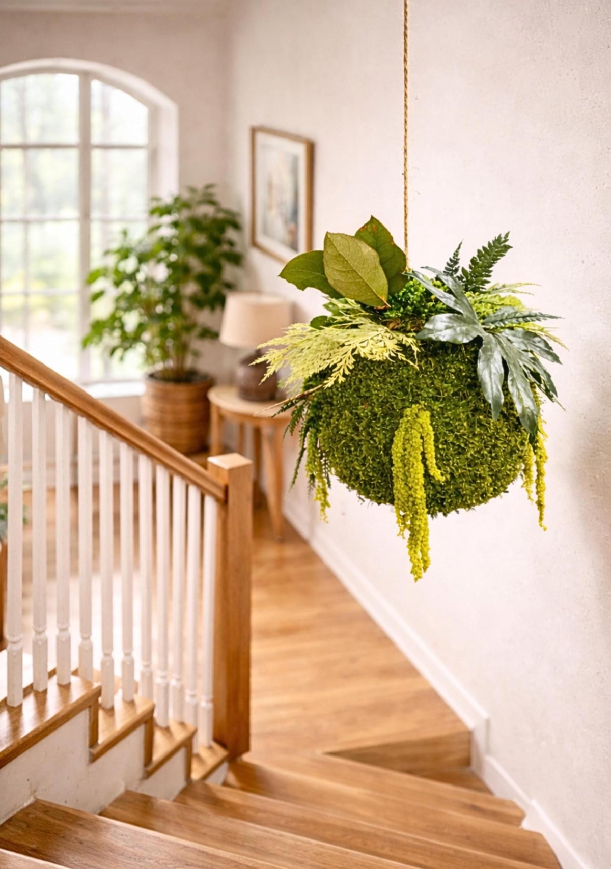 Kokedama suspendu en végétaux stabilisés, boule en mousse naturelle de 20 cm hors feuillages, feuillages retombants verts et jaune doux, suspension longue de plus d’un mètre, décoration végétale sans entretien.